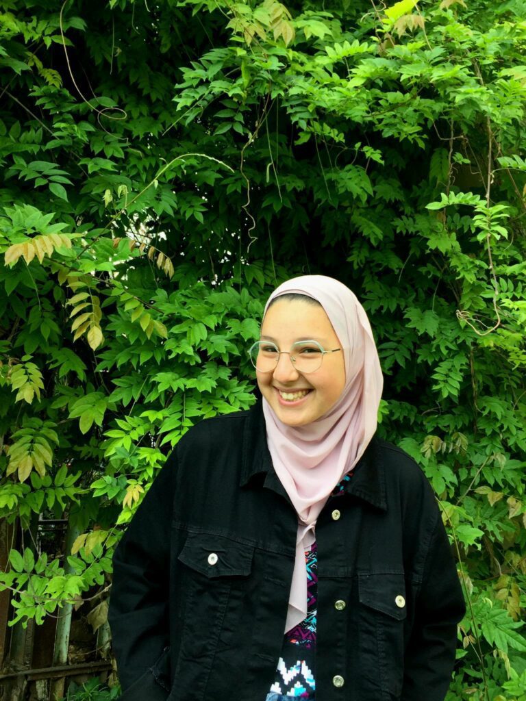 Youssra TechGirl in front of a vibrant green bush