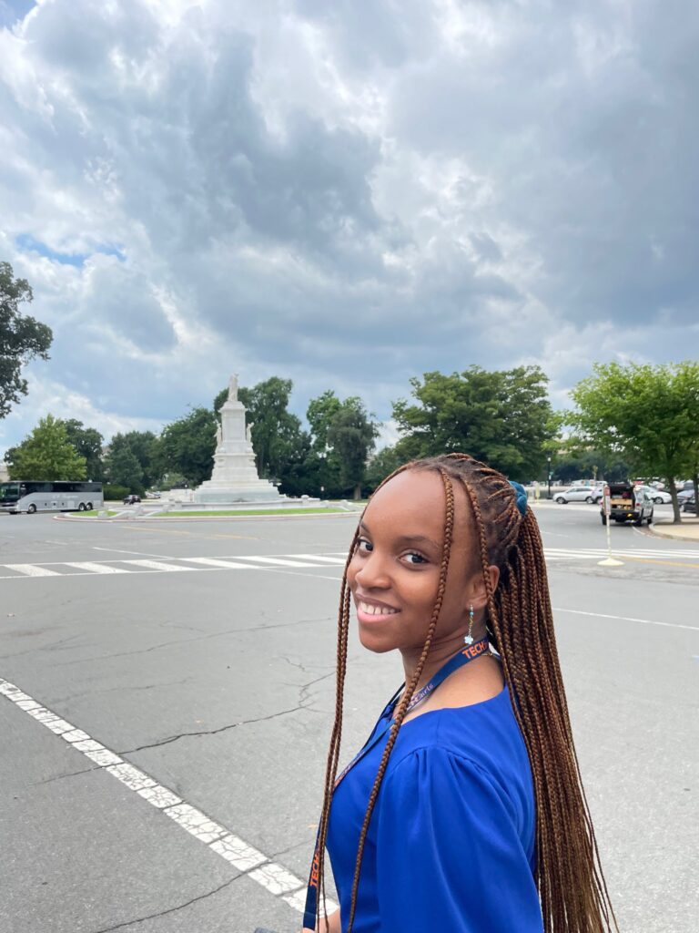 Sonia is seen with a monument, a street, and trees in the background.