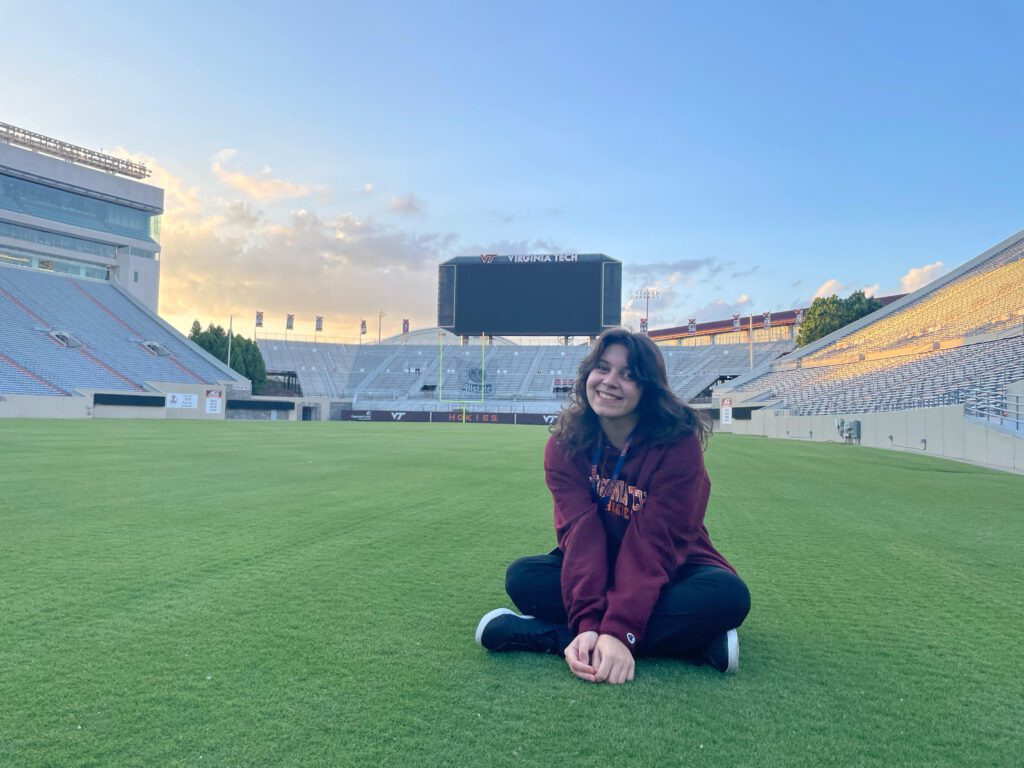 Stefania is seated on a field in a stadium