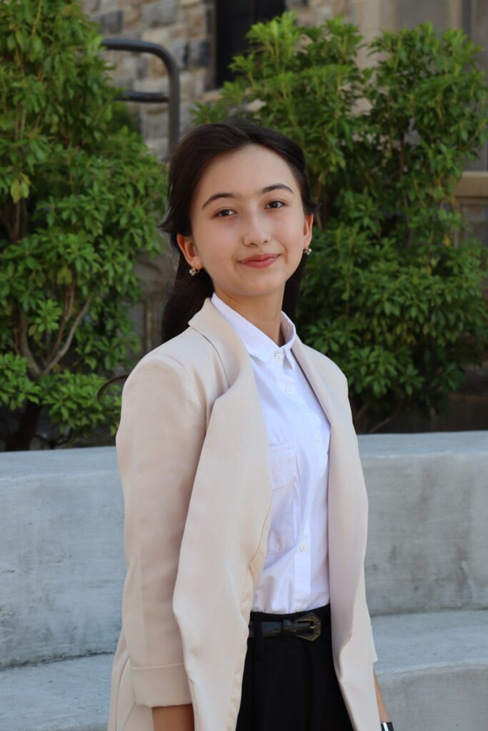 Guzalkhon smiling with shrubs behind her