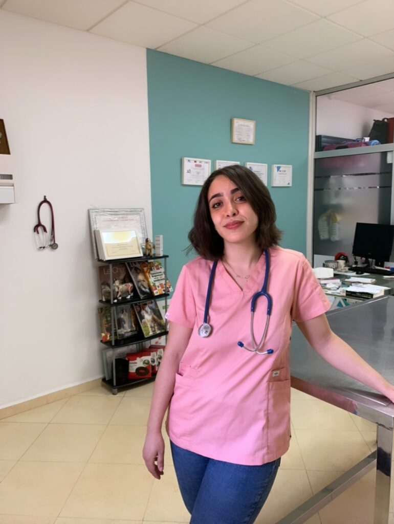 Rihab standing in veterinary clinic. She is wearing pink scrubs and a stethoscope around her neck.