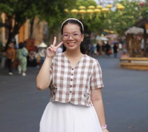 Ngan smiling in front of a blurry background. Her right hand is formed into the peace sign.