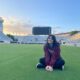Stefania is seated on a field in a stadium